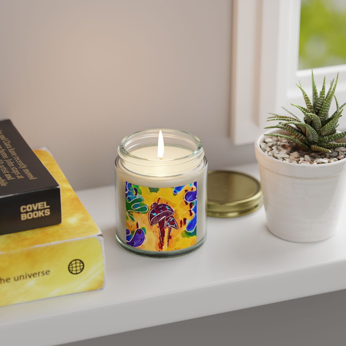 Candle with colorful label on a shelf next to a book and plant