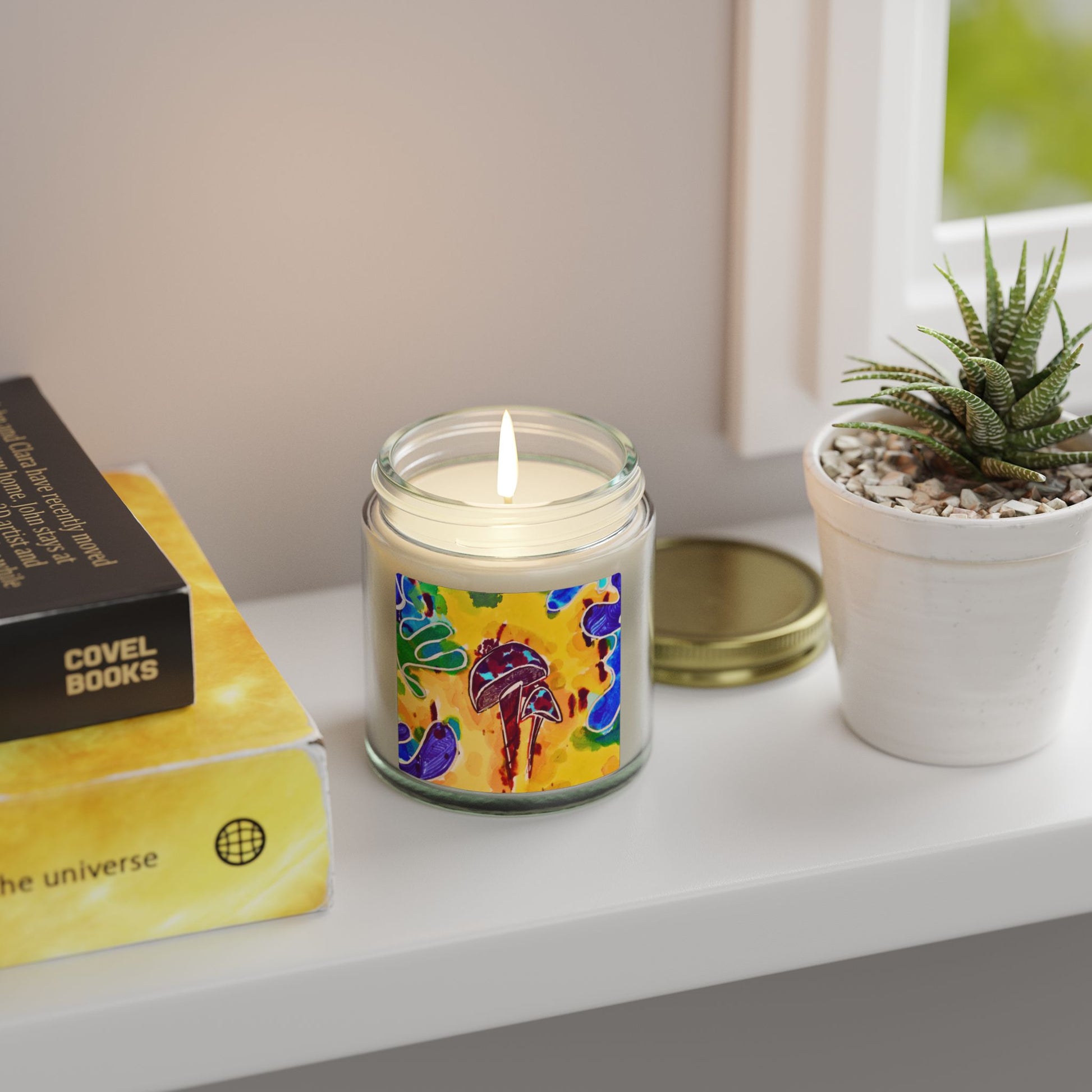 Candle with colorful label on a shelf next to a book and plant
