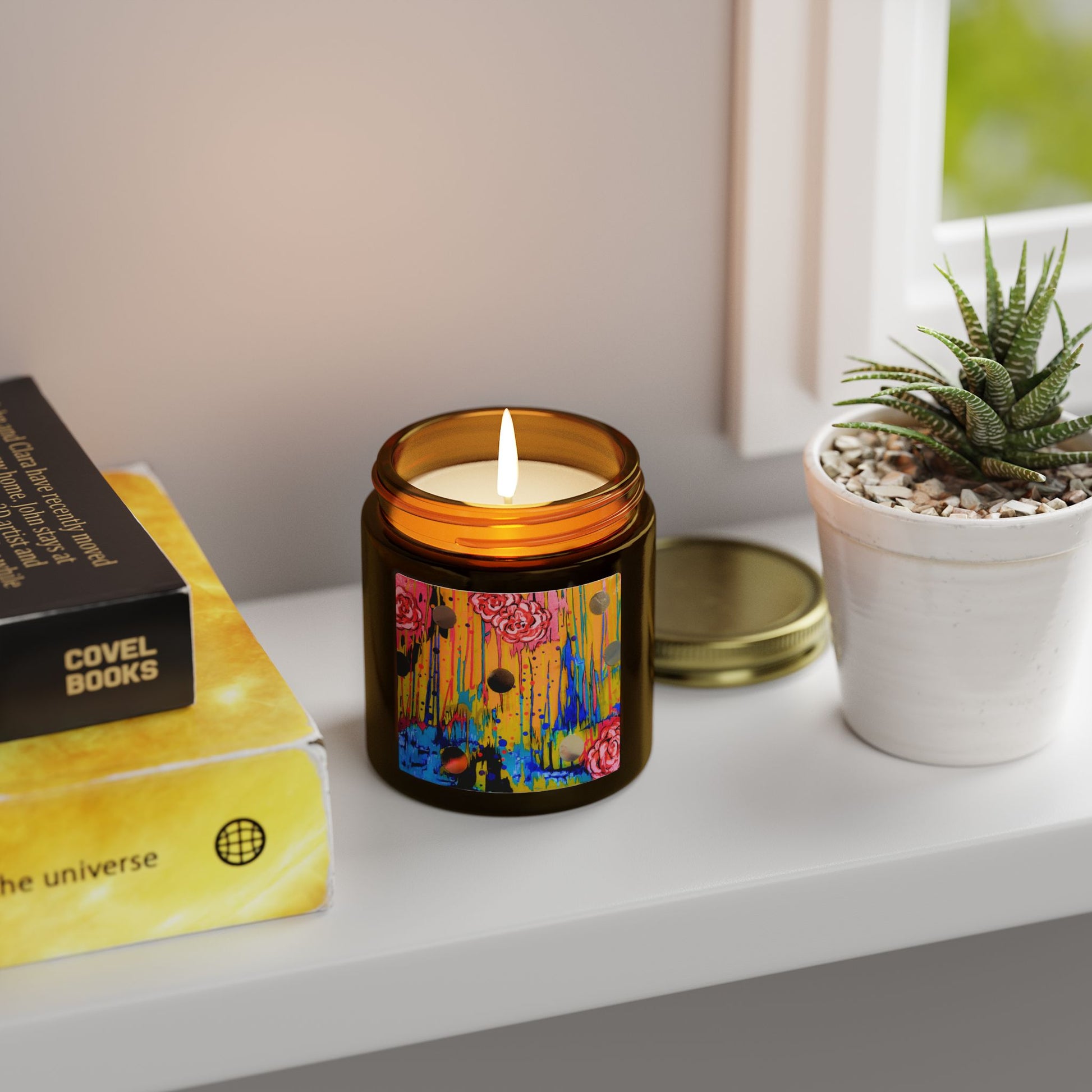 Candle with colorful design on a shelf next to books and a plant