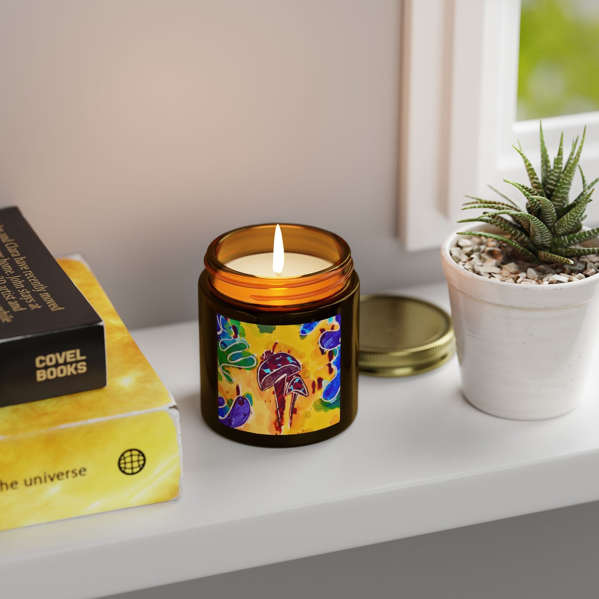 Candle with colorful label on a shelf next to a book and plant