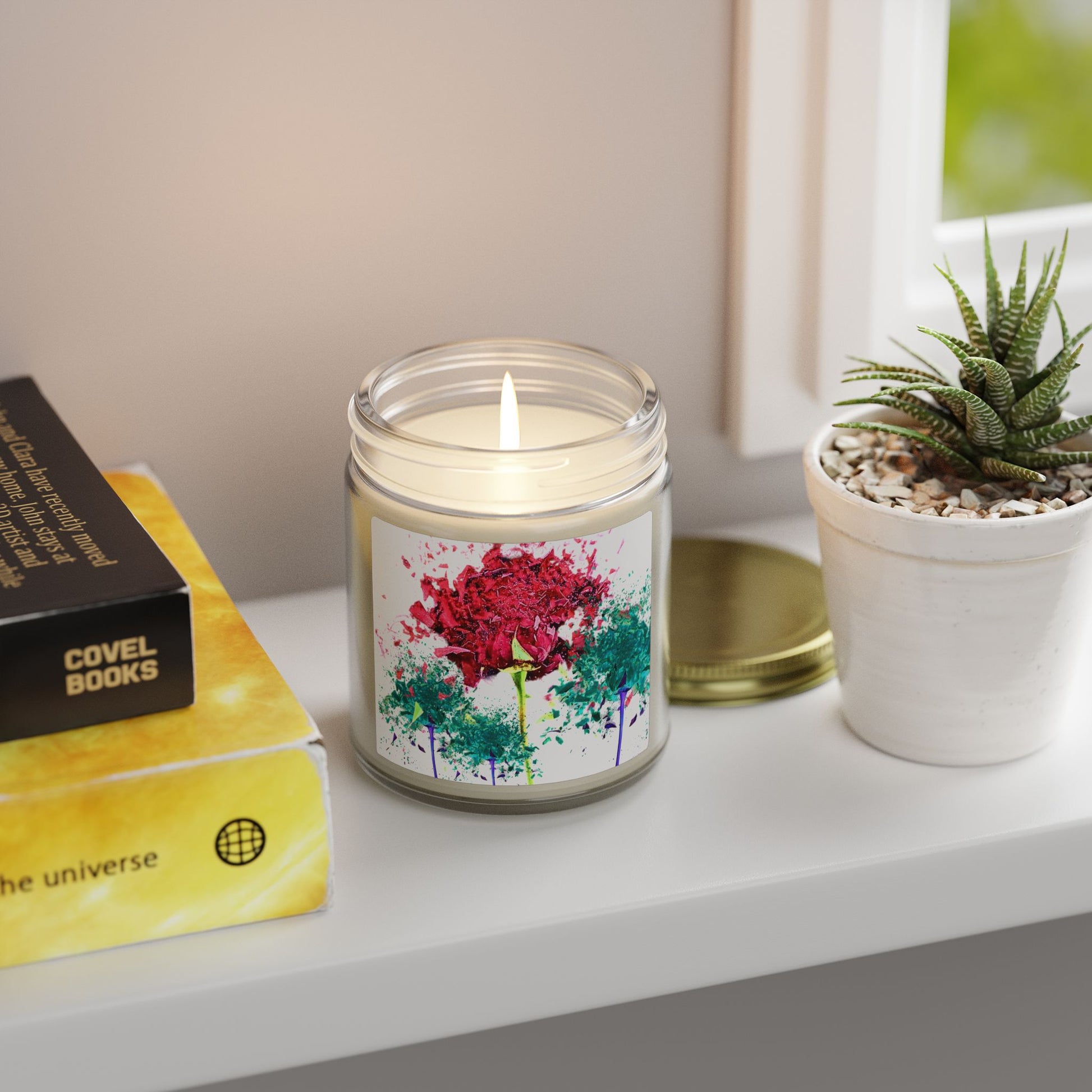 Candle with a floral design on a shelf next to a book and plant