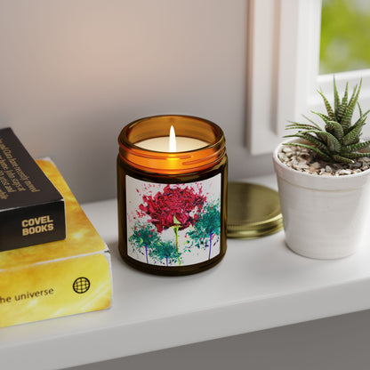 Candle in an amber jar with a colorful label on a shelf with books and a plant.