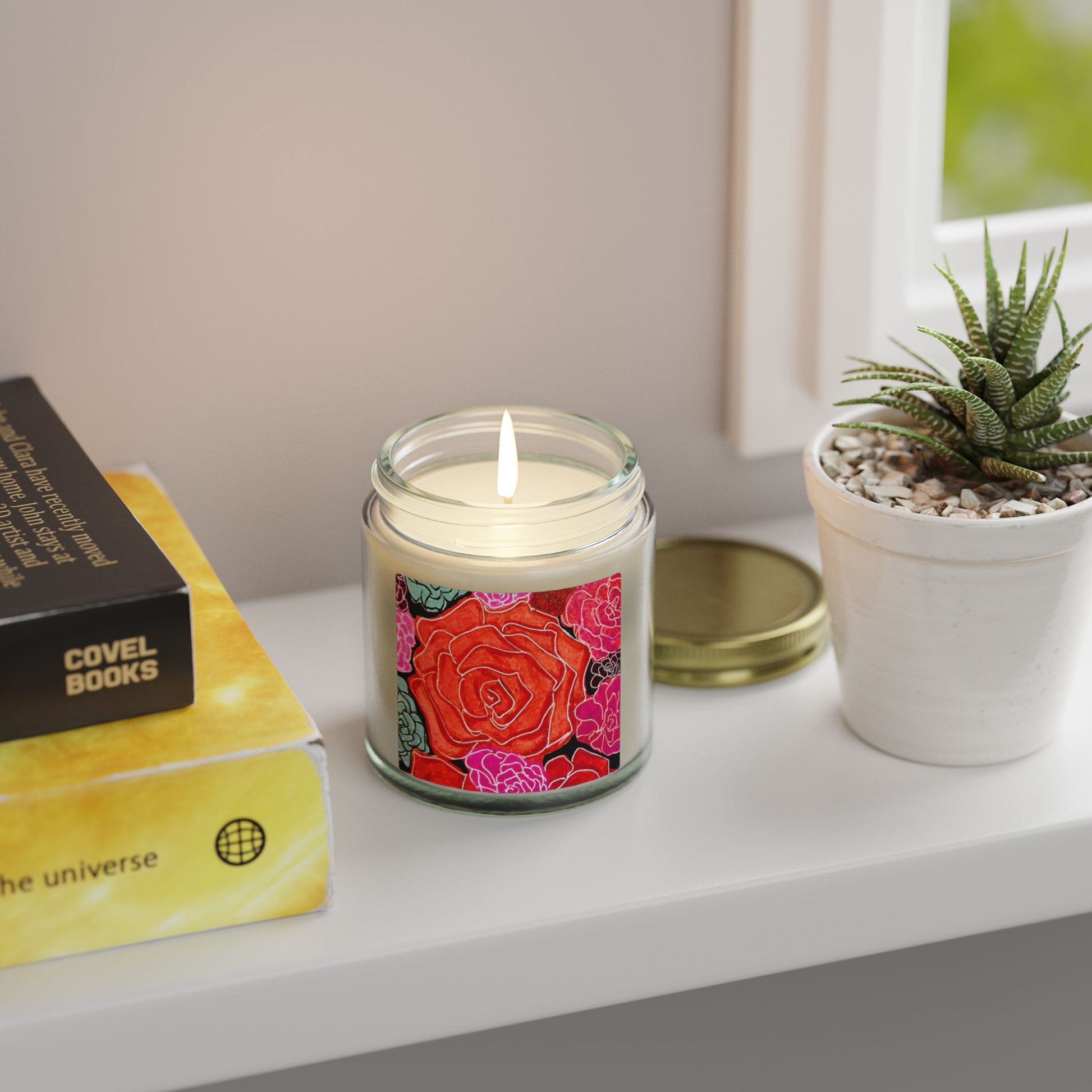 Candle with floral design on a shelf next to books and a plant