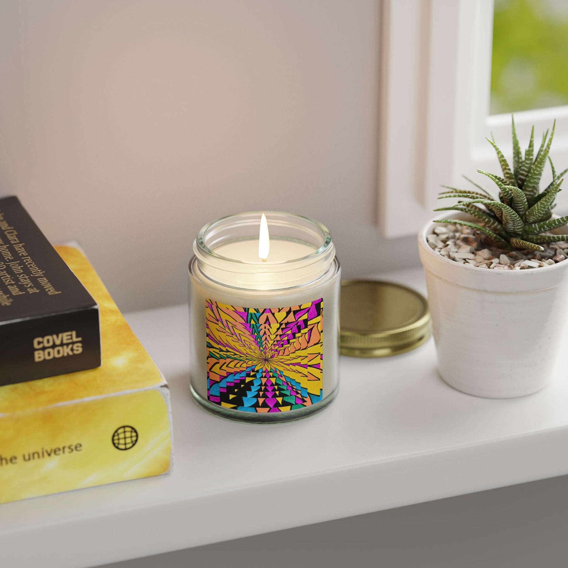Candle with colorful design on a windowsill next to books and a plant