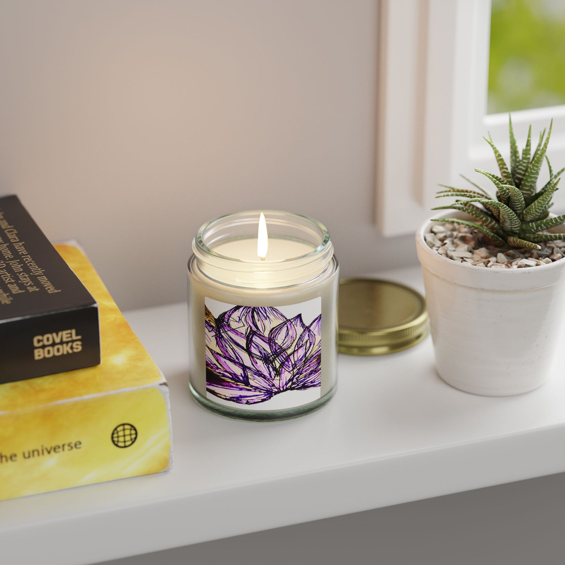 Candle with a purple flower design on a shelf next to a book and plant