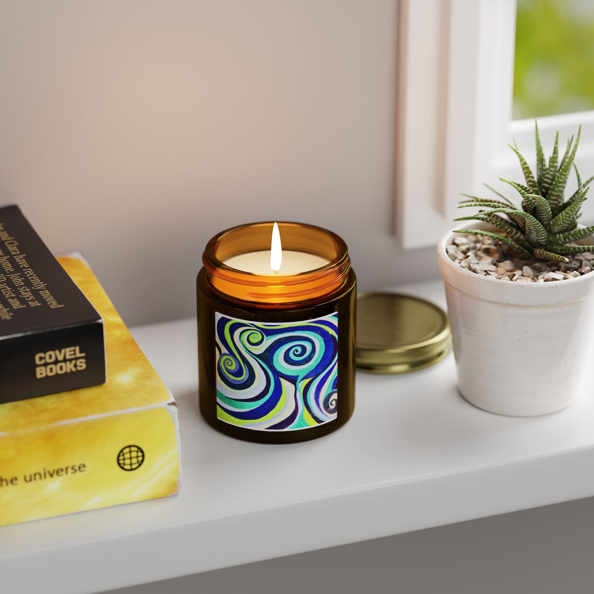 Candle with a colorful label on a shelf next to books and a plant