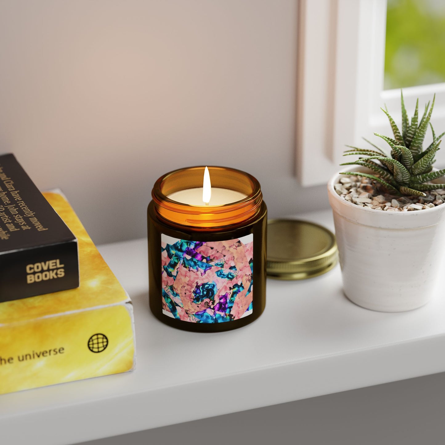 Candle with a colorful label on a shelf next to books and a plant