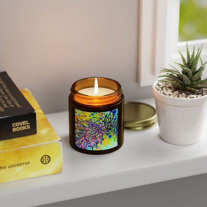Candle with colorful label on a shelf next to books and a plant
